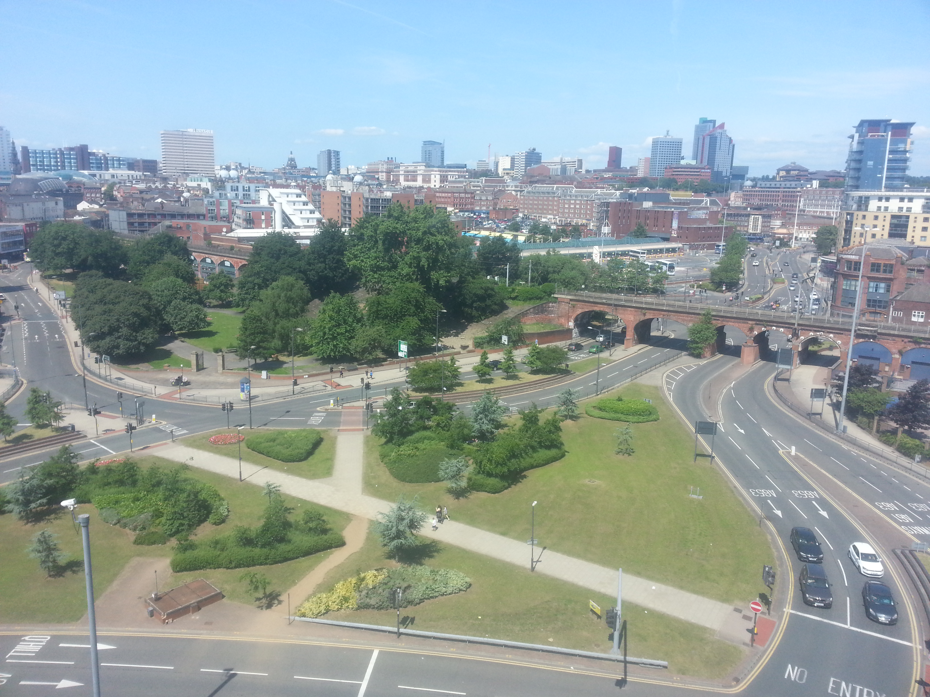 Elevated view of the Leeds skyline, with parkland and railway arches in the foreground and city towers under a clear sky.
